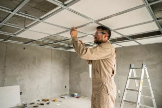 Artisan posant un faux plafond en dalles blanches sur ossature métallique dans une pièce en rénovation